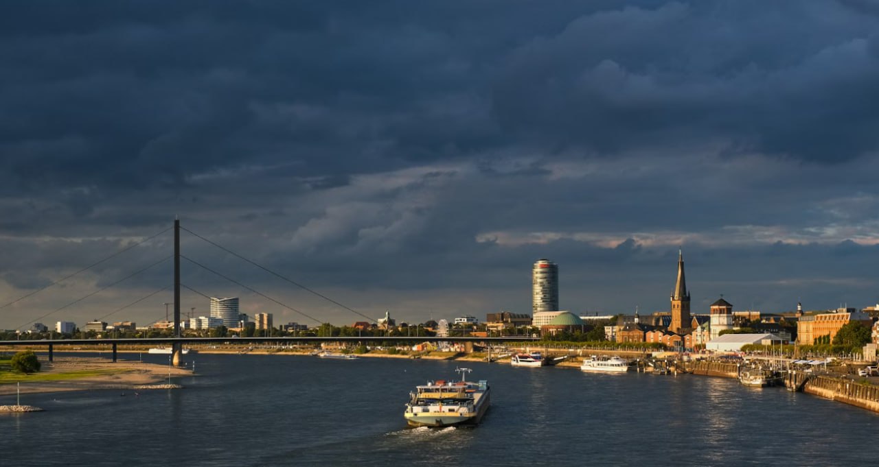 A Boat Traveling Down A River Under A Cloudy Sky