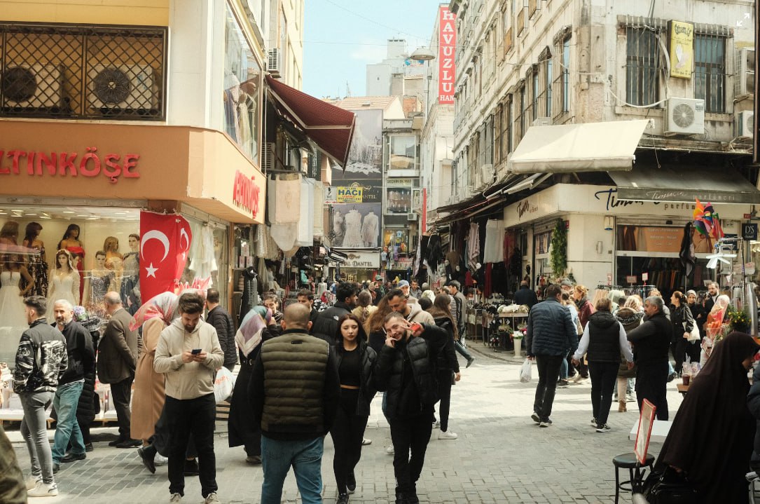A Crowd Of People Walking Down A Street Next To Tall Buildings