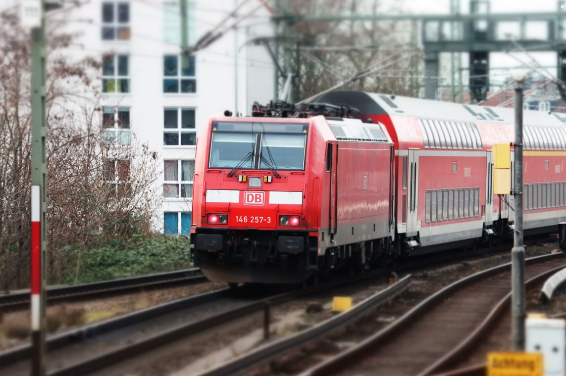 A Red Train Traveling Down Train Tracks Next To A Tall Building