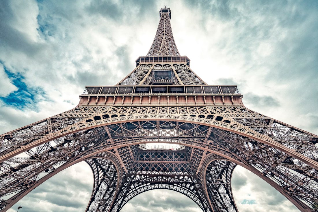 A Tall Metal Tower With Eiffel Tower In The Background