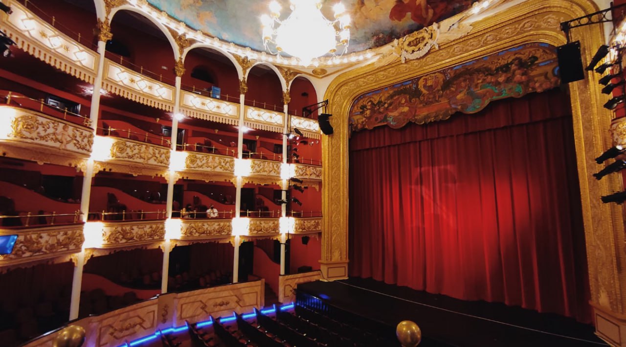 A Theater With A Red Curtain And A Chandelier