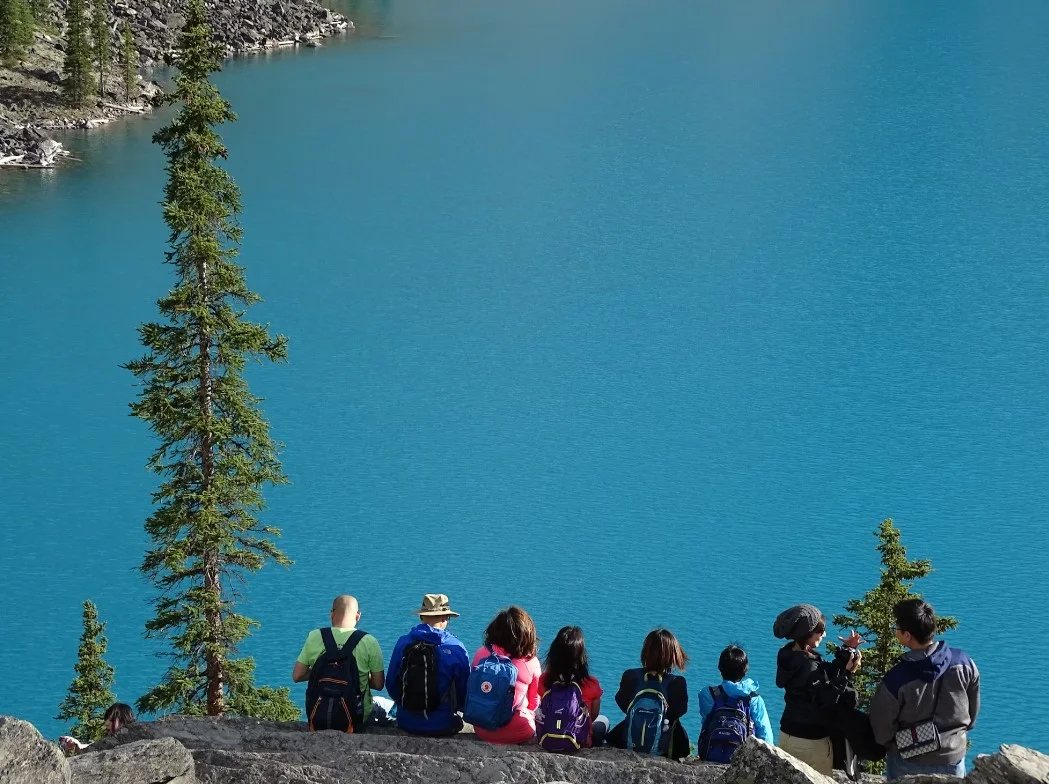 People Sitting On Rock Edge Facing Body Of Water
