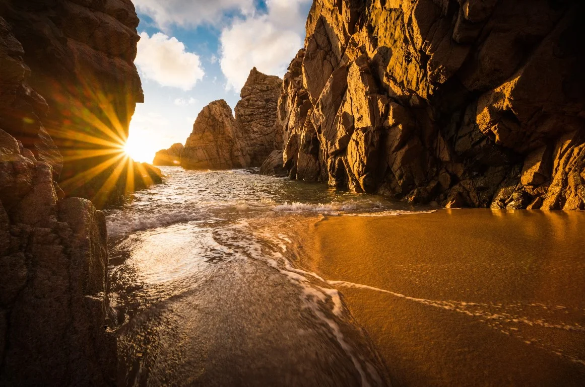The Sun Shines Brightly Through The Rocks On The Beach