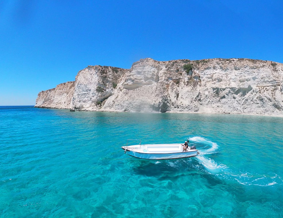 White And Blue Boat On Blue Sea Near Gray Rocky Mountain During Daytime